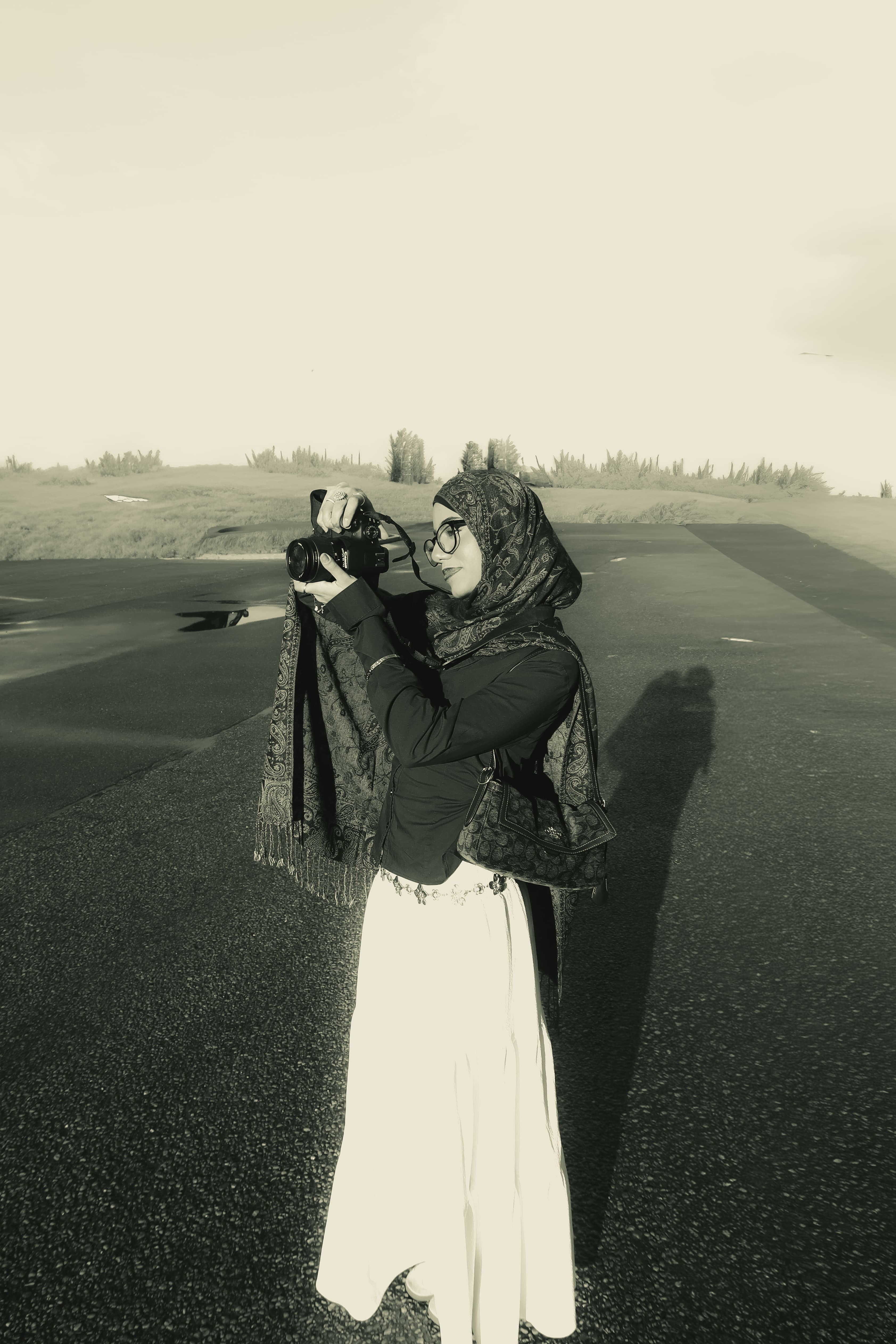Afrah photographing with her camera raised, on an open road at golden hour